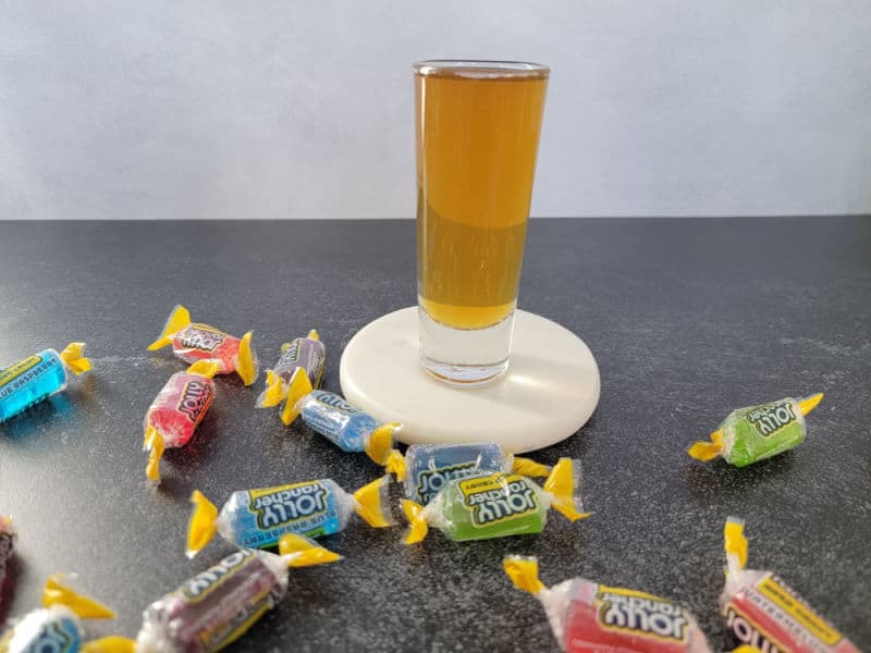 Jolly rancher shot on a white coaster surrounded by jolly rancher candy