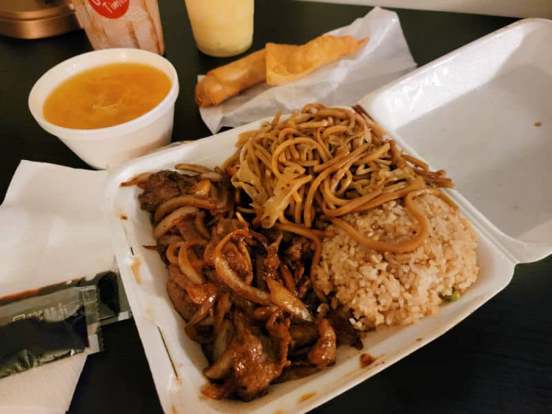 mongolian beef, noodles, fried rice in a Styrofoam container with a bowl of soup and egg roll in the background from Taste of China restaurant, Oakhurst