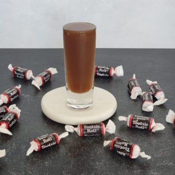 Tootsie Roll Shot on a white coaster surrounded by Tootsie Roll Candies