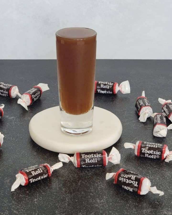 Tootsie Roll Shot on a white coaster surrounded by Tootsie Roll Candies