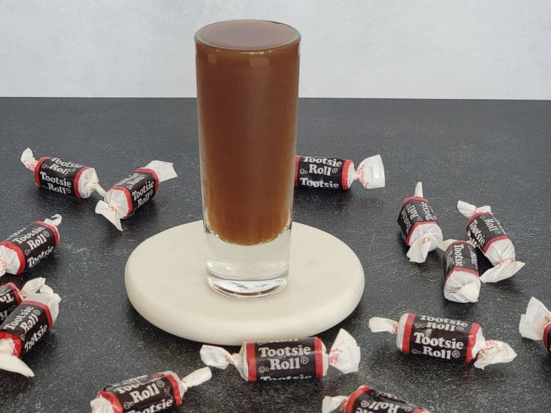 Tootsie Roll Shot on a white coaster surrounded by tootsie roll candy