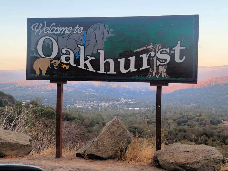 Welcome to Oakhurst wooden sign with a sequoia tree, bear, and mountains on it. 