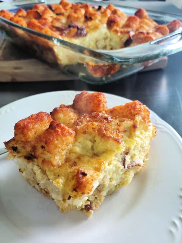 piece of tater tot breakfast casserole on a white plate near a filled casserole dish