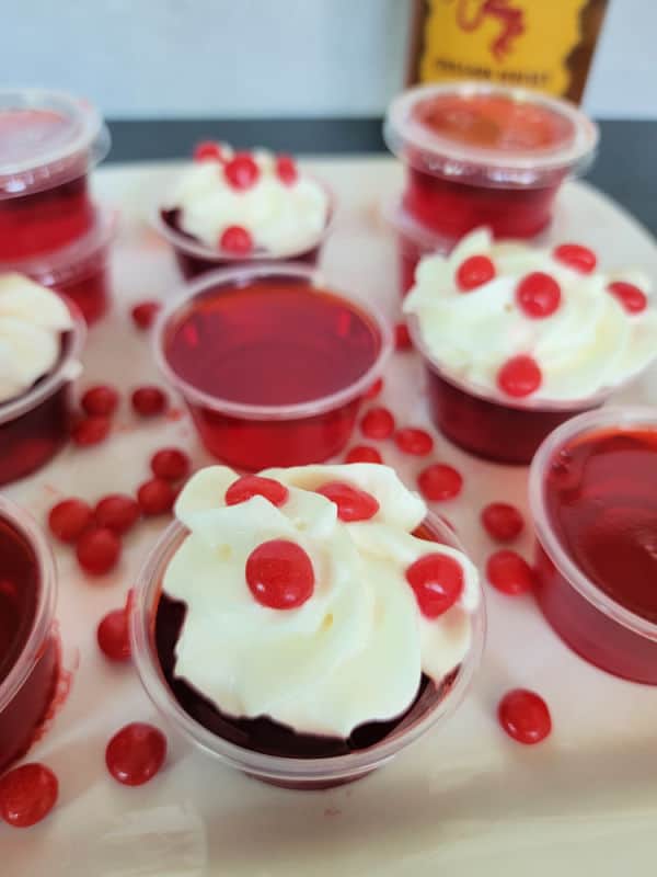 Fireball red jello shots in plastic cups garnished with whipped cream and red hots