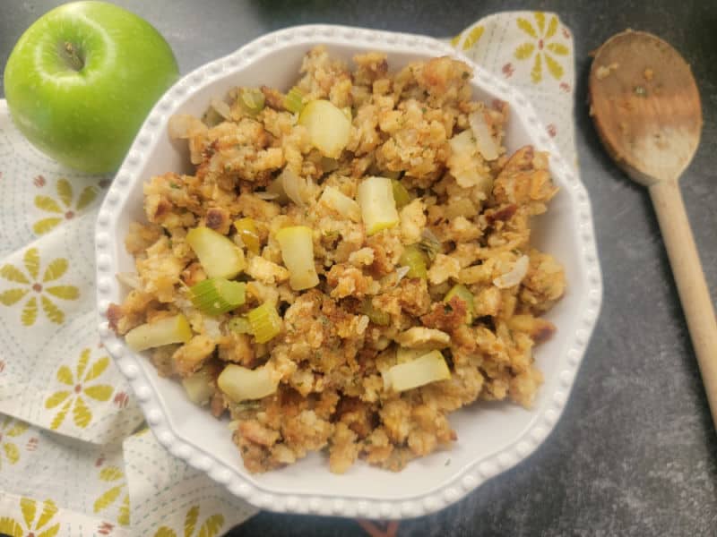 Stuffing recipe with apple served in a white bowl with a wooden spoon and green apple