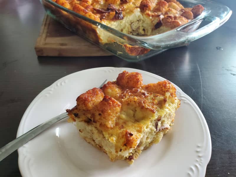 square of tater tot breakfast casserole on a white plate by a filled casserole dish