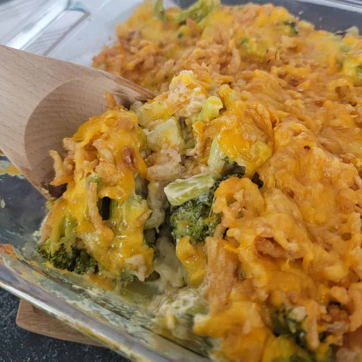 Wooden spoon scooping Broccoli Casserole from a glass baking dish