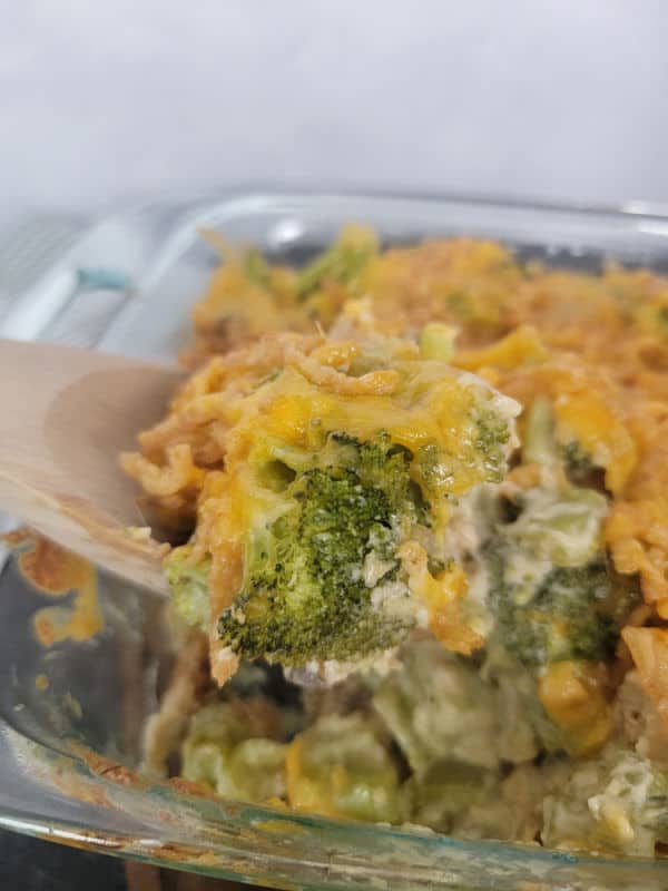 Broccoli Cheese Casserole on a wooden spoon above a casserole dish