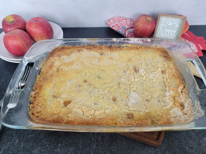 Caramel Apple Dump Cake in a glass baking dish with apples and a cloth towel