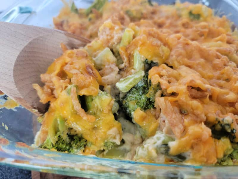 wooden spoon scooping cheesy broccoli casserole from a glass baking dish