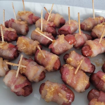 Brown sugar coated bacon wrapped little smokies with toothpicks on a white platter