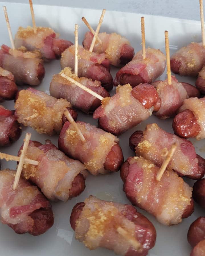 Brown sugar coated bacon wrapped little smokies with toothpicks on a white platter