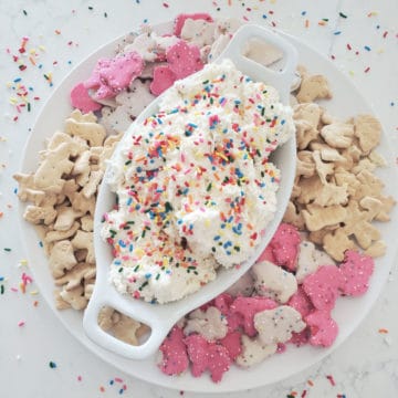 Dunkaroo dip in a white bowl surrounded by animal crackers and cookies and rainbow sprinkles