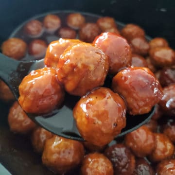 Grape jelly meatballs on a plastic serving spoon above a slow cooker
