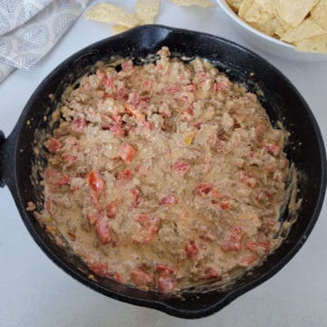 Velveeta Rotel Dip in a cast iron skillet next to a bowl of chips