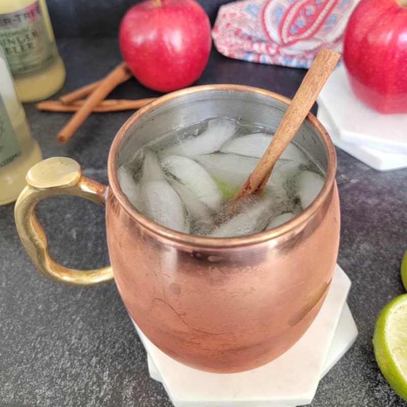 Apple Cider Mule in a copper mug next to apples and ginger beer
