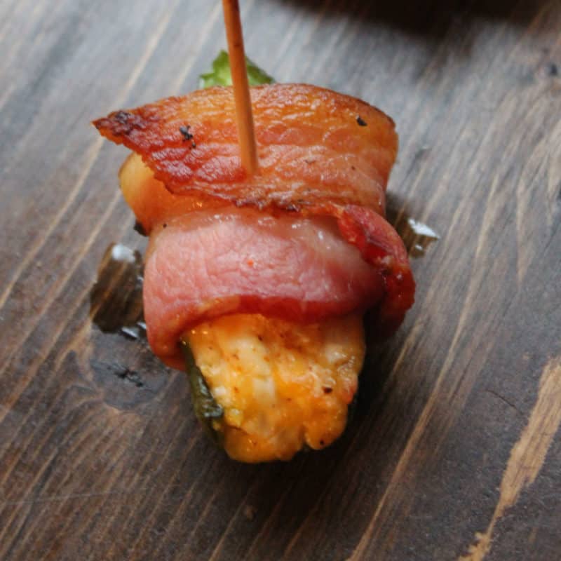 Bacon-Wrapped Jalapeños with a toothpick holding it on a wood board