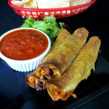Corn and Black Bean Baked Taquitos on a black plate next to salsa