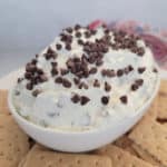 Booty dip covered in mini chocolate chips in a white bowl surrounded by graham crackers
