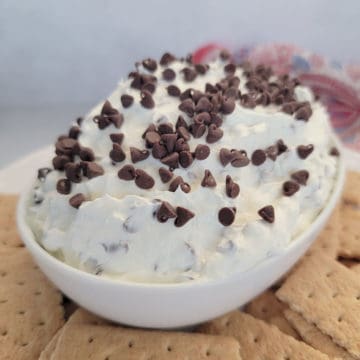 Booty dip covered in mini chocolate chips in a white bowl surrounded by graham crackers
