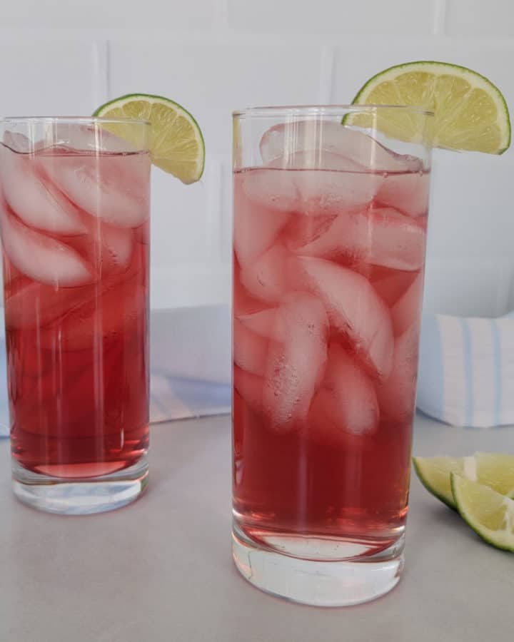 Two red Woo Woo Drinks in tall glasses wtih lime wedges next to a cloth napkin