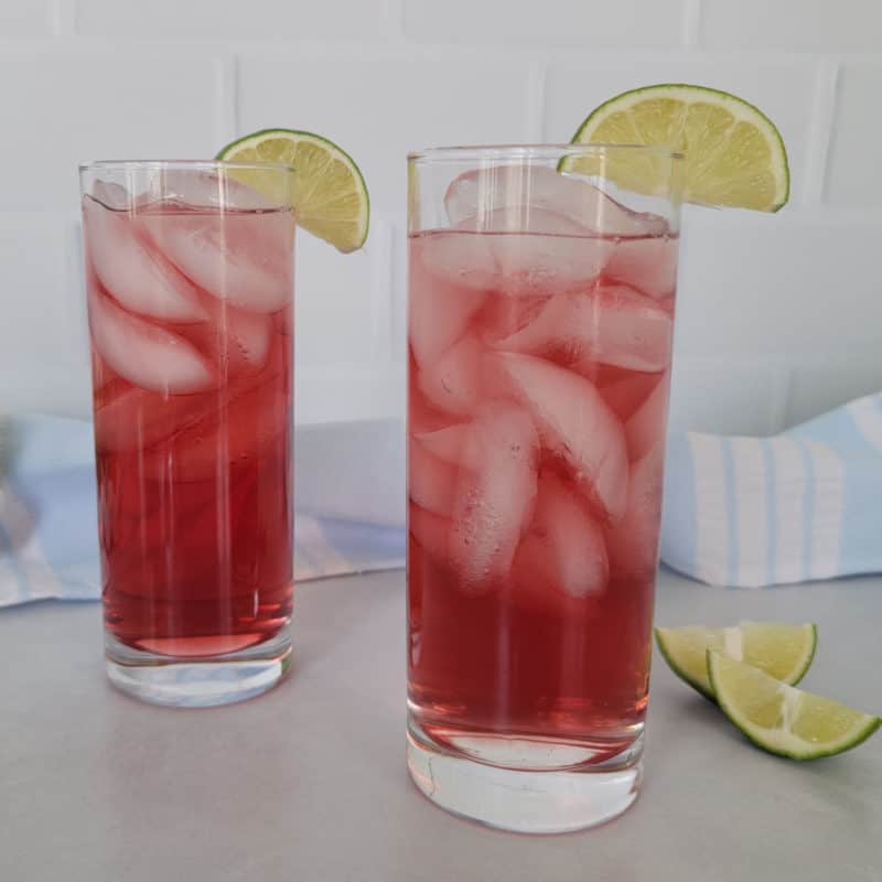 Two red Woo Woo Drinks in tall glasses wtih lime wedges next to a cloth napkin