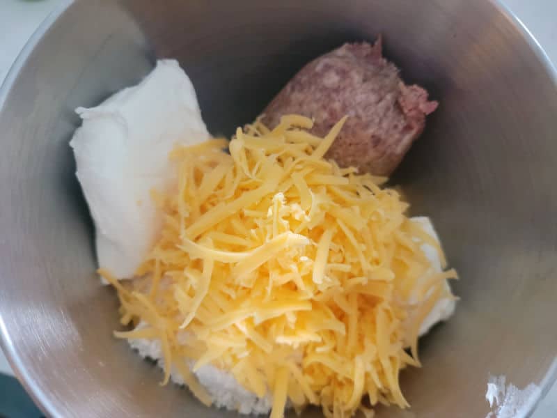 Cheddar Bay sausage ball ingredients shredded cheese, ground sausage, biscuit mix, and cream cheese in mixer bowl