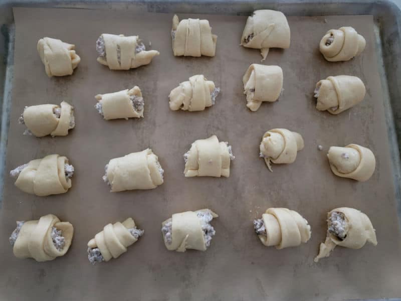 Crescent rolls filled with sausage and cream cheese on a baking sheet