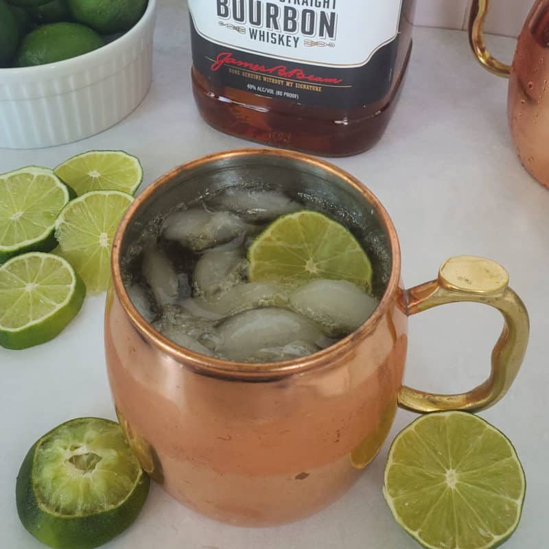 Kentucky Mule with lime circles in a copper mug next to a bottle of kentucky bourbon