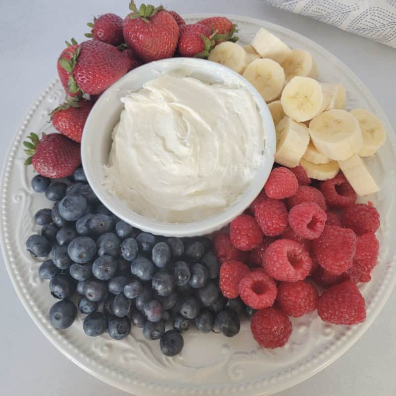 Marshmallow Fluff Fruit Dip in a white bowl surrounded by blueberries, raspberries, bananas, and strawberries 