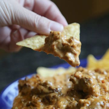 meat lovers queson on a tortilla chip above a bowl full of queso