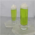 two bright green Scooby Snack Shots with whipped cream garnish