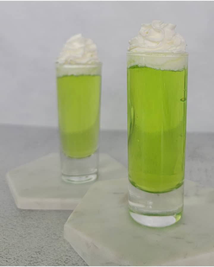 two bright green Scooby Snack Shots with whipped cream garnish