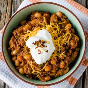 Crock Pot Spicy Bacon & Beef Chili garnished with sour cream in a bowl on a cloth napkin