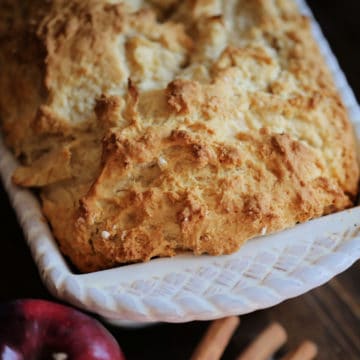 Apple Beer Bread in a white baking dish next to an apple and cinnamon sticks