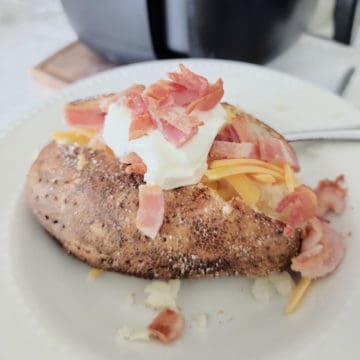 Air fryer baked potato topped with sour cream, bacon, and cheddar cheese