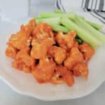 Air Fryer buffalo cauliflower on a white plate with celery next to a cloth napkin