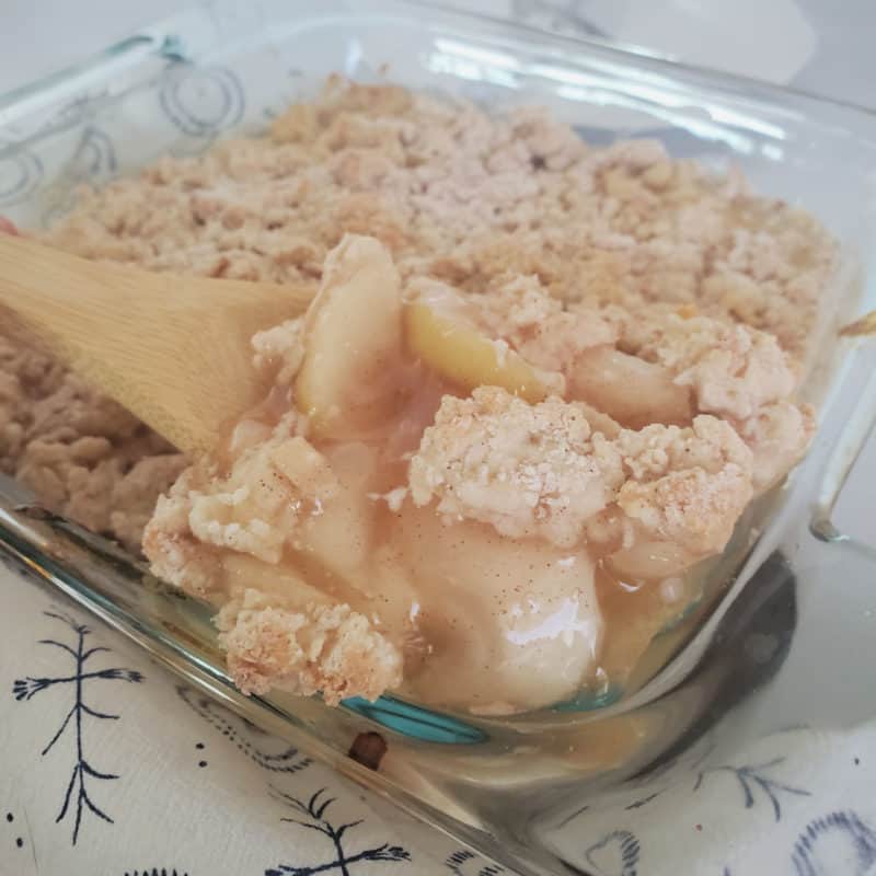 Bisquick Apple Cobbler in a glass baking dish with a wooden spoon scooping out some cobbler