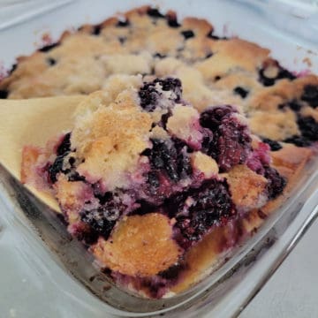 Bisquick Blackberry cobbler in a glass baking dish with a wooden spoon scooping cobbler out