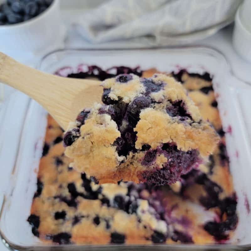 Bisquick Blueberry Cobbler on a wooden spoon above a baking dish