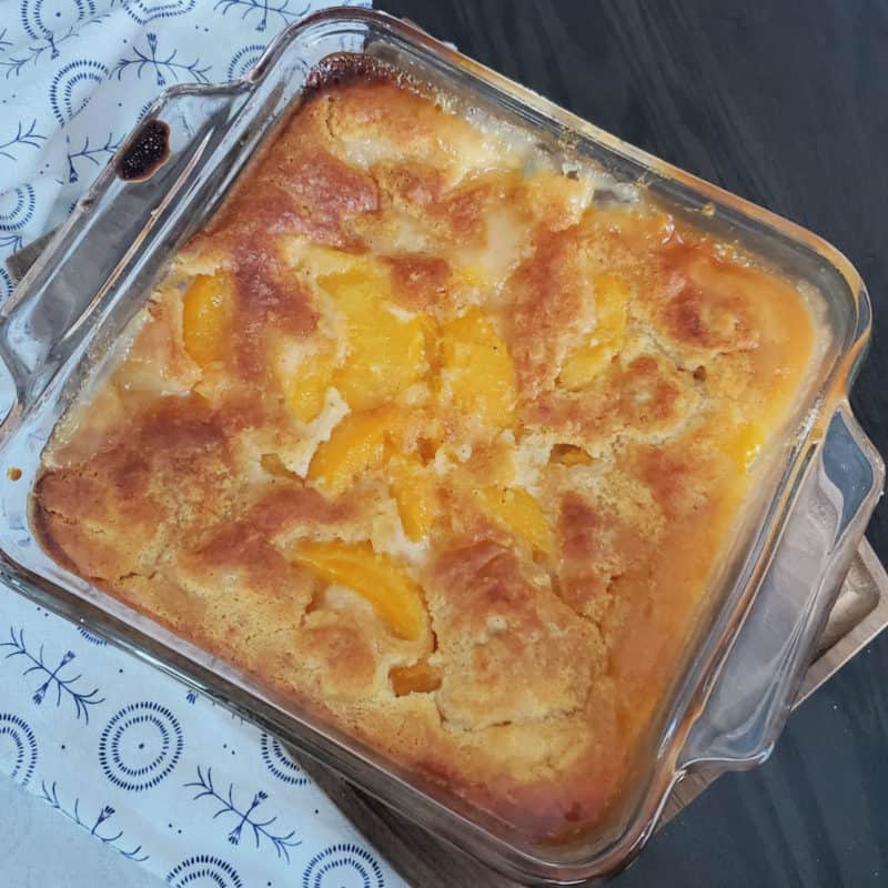 Bisquick Peach Cobbler in a glass baking dish by a cloth napkin
