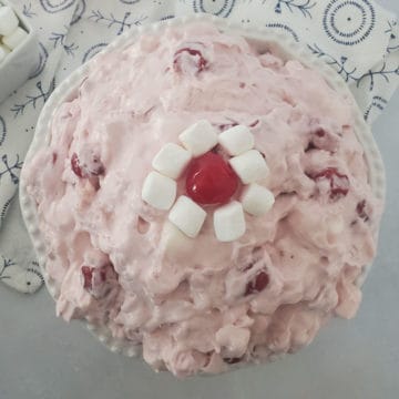 Cherry fluff salad in a white bowl garnished with mini marshmallows and a maraschino cherry