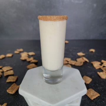 Cinnamon Toast Crunch Shot in a tall shot glass on white coasters surrounded by cereal