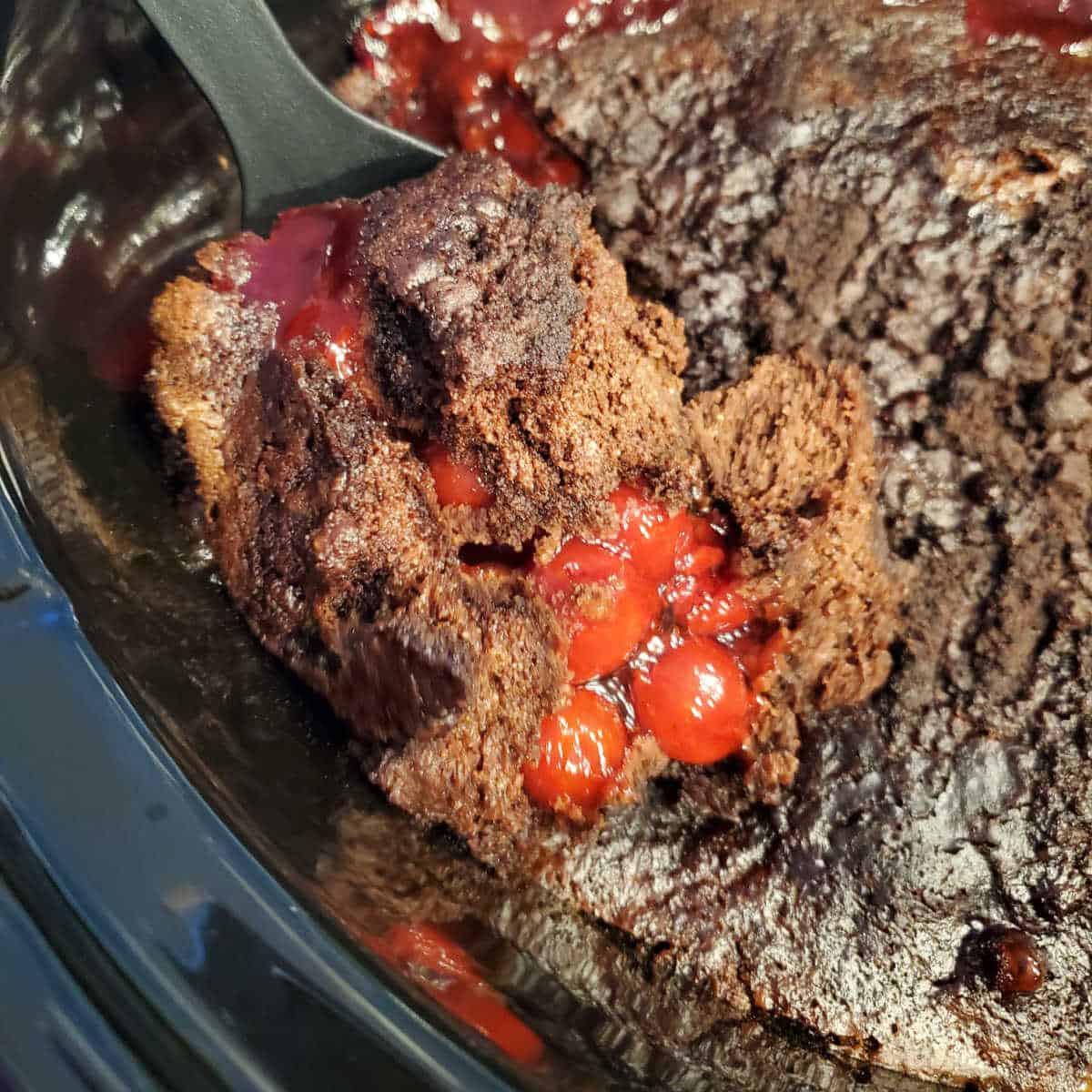 Crock Pot Chocolate Cherry Dump Cake on a spoon above a slow cooker