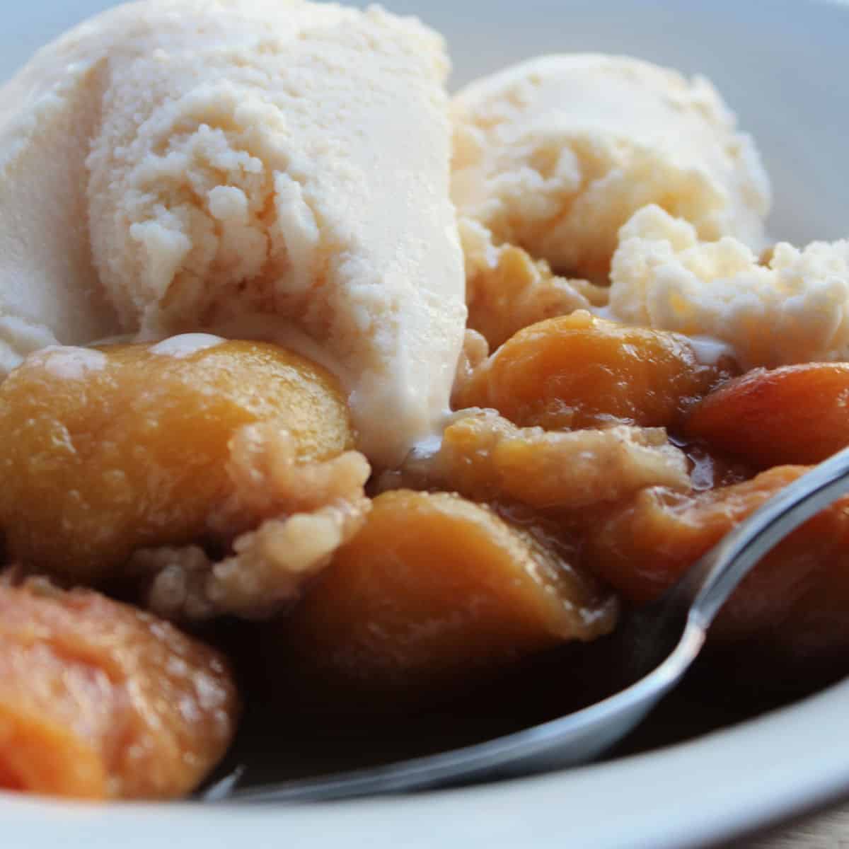 peach crumble topped with vanilla ice cream in a white bowl