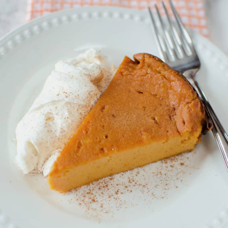 pumpkin pie pudding cake on a white plate with whipped cream and a fork