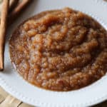 Crockpot applesauce in a white bowl next to a couple of cinnamon sticks