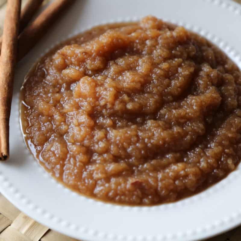 Crockpot applesauce in a white bowl next to a couple of cinnamon sticks