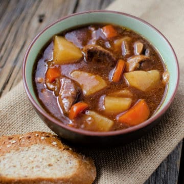 Guinness stew with potatoes and carrots in a bowl next to a slice of bread