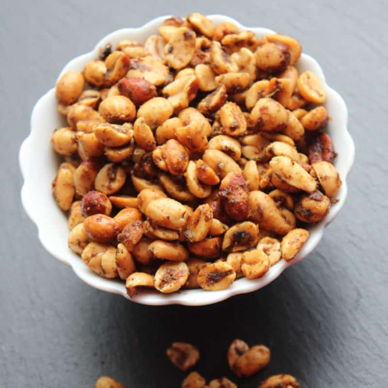 Spicy peanuts in a white bowl with a few below the bowl